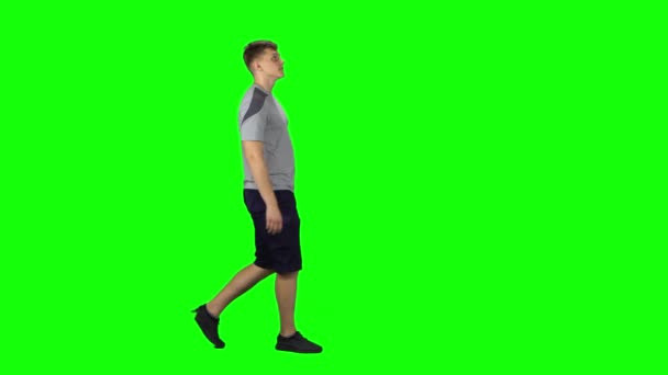 Mladý muž kráčí po zelené obrazovce. Boční pohled profilu — Stock video