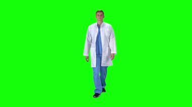 Medical man in white coat going and looking forward against a green background. Slow motion.