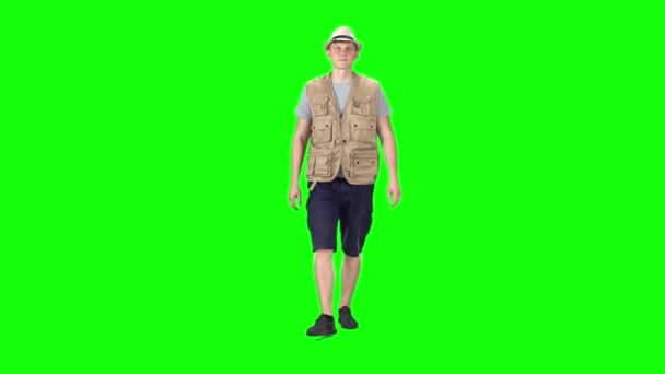 Fiatal férfi szürke pólóban, ujjatlan ingben, rövidnadrágban, tornacipőben és kalapban, zöld háttérrel. Lassú mozgás.. — Stock videók