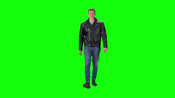 Young man in black leather jacket, jeans and sneakers going against a green background. Slow motion. — Stock Video