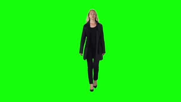 Chica rubia con abrigo negro, pantalones y zapatos de tacón alto que van contra una pantalla verde. Movimiento lento — Vídeo de stock