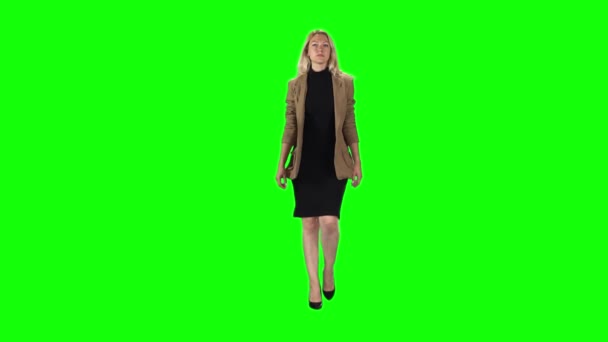 Ξανθιά κοπέλα σε ένα κομψό καφέ σακάκι, μαύρο φόρεμα και ψηλοτάκουνα παπούτσια πηγαίνει ενάντια σε μια πράσινη οθόνη. Αργή κίνηση — Αρχείο Βίντεο