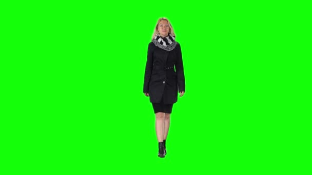 Chica rubia en un vestido negro, abrigo, bufanda y botas que van contra una pantalla verde. Movimiento lento — Vídeo de stock