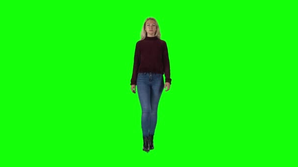 Блондинка в гранатовом свитере, джинсах и сапогах идет против зеленого экрана. Медленное движение — стоковое видео