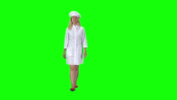 Cozinha loira chef em uniforme branco e chapéu indo contra uma tela verde. Movimento lento — Vídeo de Stock