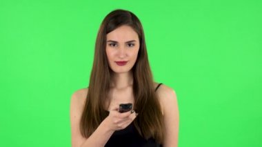 Elinde uzaktan kumandalı bir kadın, televizyonu açıyor ve çok gülüyor. Yeşil ekran. Yeşil Ekran