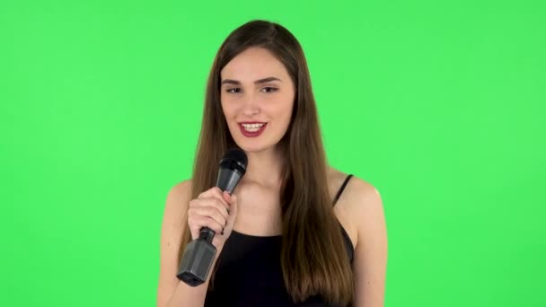Привлекательная девушка поет в микрофон и переходит к ритму музыки. Зеленый экран — стоковое видео
