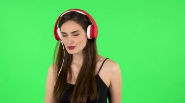 Neşeli kız dans ediyor ve büyük kırmızı kulaklıklarla müzik dinlemekten hoşlanıyor. Yeşil Ekran