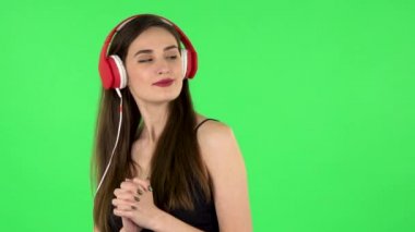 Neşeli kız dans ediyor ve büyük kırmızı kulaklıklarla müzik dinlemekten hoşlanıyor. Yeşil Ekran