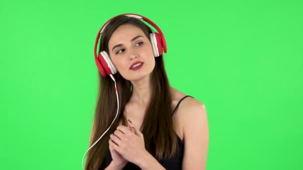 Χαρούμενο κορίτσι που χορεύει και απολαμβάνει τη μουσική με μεγάλα κόκκινα ακουστικά. Πράσινη οθόνη — Αρχείο Βίντεο