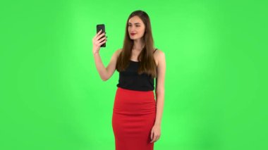 Gülümseyen kız görüntülü konuşma için cep telefonu kullanıyor ve yeşil ekranda seviniyor.