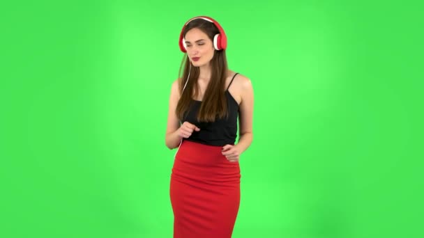 Chica alegre bailando y disfruta de la música en grandes auriculares rojos. Pantalla verde — Vídeos de Stock