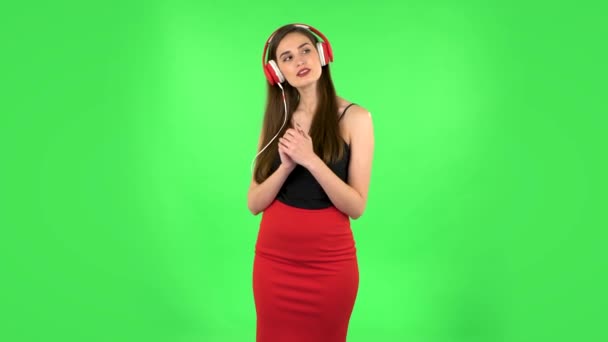 Cheerful girl dancing and enjoys music in big red headphones. Green screen — Stock Video