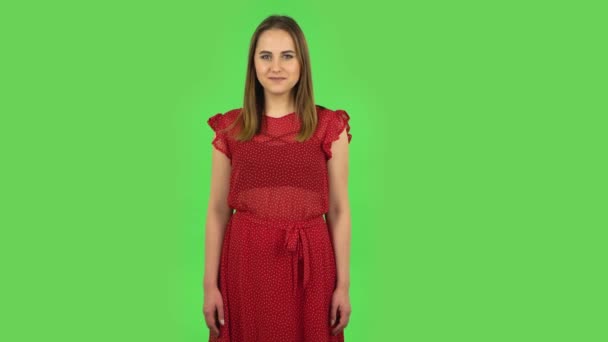 Chica tierna en vestido rojo es coqueta sonriendo mientras mira a la cámara. Pantalla verde — Vídeos de Stock