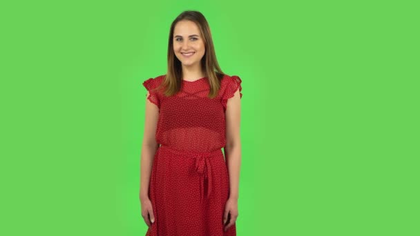 Нежная девушка в красном платье кокетливо улыбается, глядя в камеру. Зеленый экран — стоковое видео