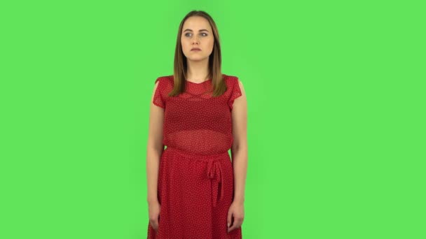 Tender girl in red dress is looking around, covering her mouth with her hand and whispering the secret. Green screen — Wideo stockowe