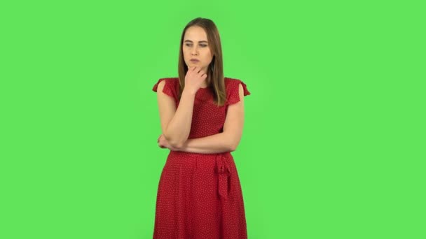 Нежная девушка в красном платье о чем-то думает. Зеленый экран — стоковое видео