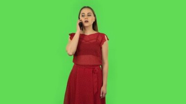 Tender girl in red dress is talking for mobile. Green screen