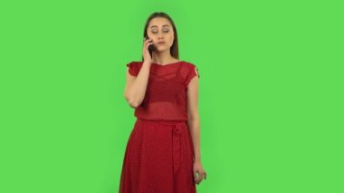 Tender girl in red dress is talking for mobile. Green screen