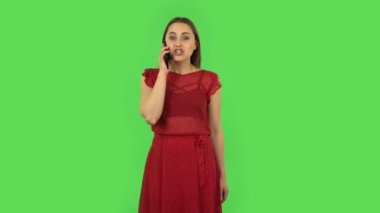Tender girl in red dress is talking for mobile and shocked then rejoice. Green screen