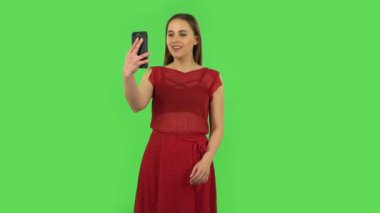 Tender girl in red dress is talking for video chat using mobile phone and dissatisfied. Green screen