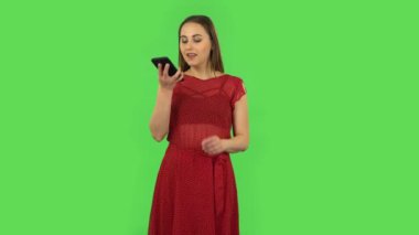 Tender girl in red dress is asking for information on the network via phone. Green screen