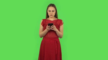 Tender girl in red dress is texting on her phone. Green screen