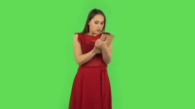 Tender girl in red dress is angrily writing with pencil in notebook. Green screen