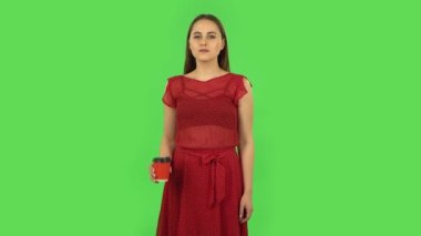 Tender girl in red dress drinking unpalatable coffee and is disgusted. Green screen