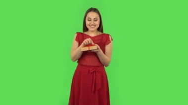 Tender girl in red dress is opening the gift, very surprised and upset. Green screen