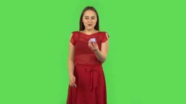Tender girl in red dress is opening a small box with a surprise and is very rejoicing, saying yes. Green screen
