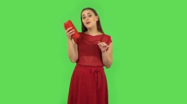 Tender girl in red dress is listening to music with bluetooth portable speaker and dancing. Green screen
