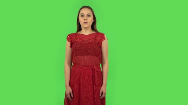 Ніжна дівчина в червоній сукні уважно розглядає щось, потім страшно прикриває обличчя рукою. Зелений екран — стокове відео