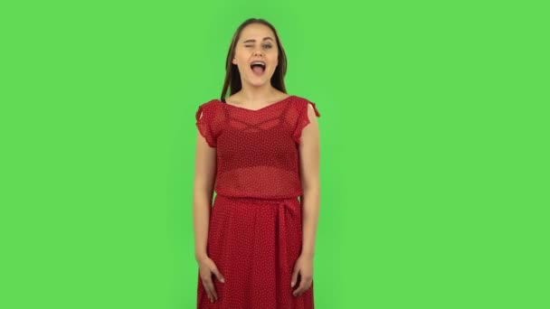 Het tedere meisje in rode jurk glimlacht breed en knipoogt. Groen scherm — Stockvideo