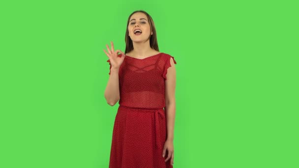 Ніжна дівчина в червоній сукні робить знак добре. зелений екран — стокове відео