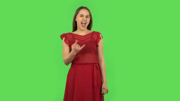Gyengéd lány piros ruhában tesz egy rock gesztust, és élvezi az életet. Zöld képernyő — Stock videók