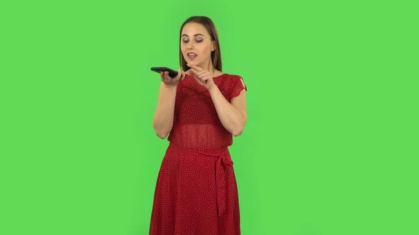 Tender girl in red dress is asking for information on the network via phone. Green screen — Stok video