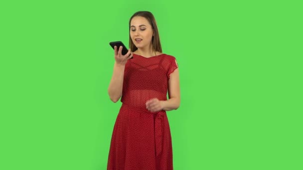 Tender girl in red dress is asking for information on the network via phone. Green screen — Wideo stockowe