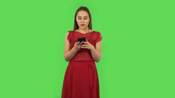 Tender happy girl in red dress is texting on her phone. Green screen — 图库视频影像