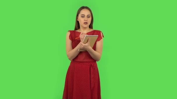 Tender girl in red dress is standing and thinking, then happy writing with pencil in notebook. Green screen — Stok video