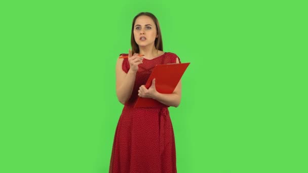 Tender girl in red dress fills papers in red folder with pensil. Green screen — Stockvideo