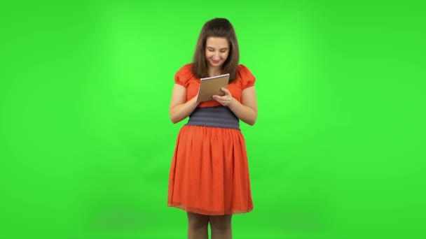Cute girl is thinking, then happy writing with pencil in notebook. Green screen — Stock Video