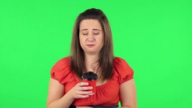 Portrait of cute girl is drinking unpalatable coffee and is disgusted. Green screen
