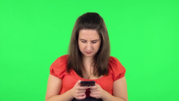 Portrait of cute girl angrily texting on her phone. Green screen — Stockvideo