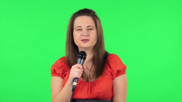 Portrait of cute girl is singing into a microphone and moving to the beat of music. Green screen — Stockvideo