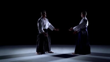 Aikido hakama 'nın özel kıyafetleri içinde iki usta katılımcı sahne ışıkları üzerinde tekli dövüş yöntemleri üzerinde çalışırlar..
