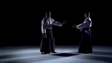 Aikido hakama 'nın özel kıyafetleri içinde iki usta katılımcı sahne ışıkları üzerinde tekli dövüş yöntemleri üzerinde çalışırlar..