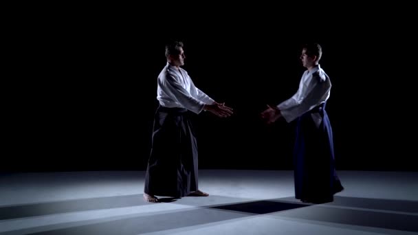 Two Masters participants of the training in special clothes of aikido hakama work out the methods of single combat on spotlights background. — Stock Video
