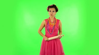 Girl with a rolling pin in her hands angry looks at the camera. Green screen
