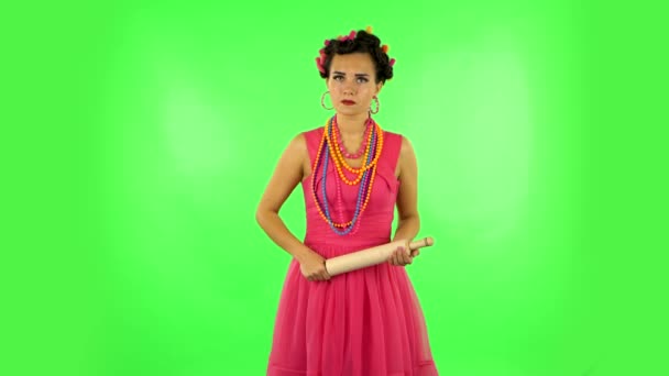 Girl with a rolling pin in her hands angry looks at the camera. Green screen — Stockvideo